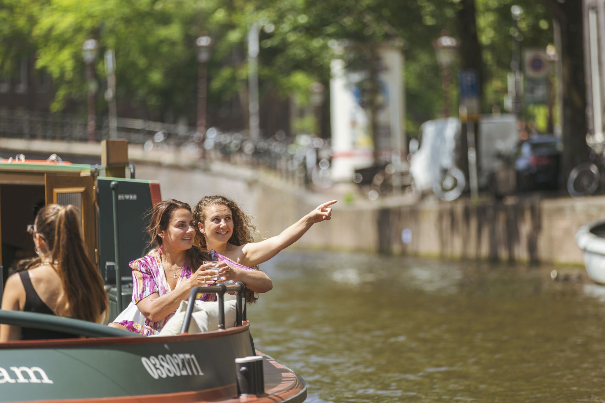 Boaty.nl - Twee vrouwen op een boot Zwei Frauen genießen eine Grachtenfahrt in Amsterdam; eine von ihnen zeigt begeistert auf etwas in der Ferne.