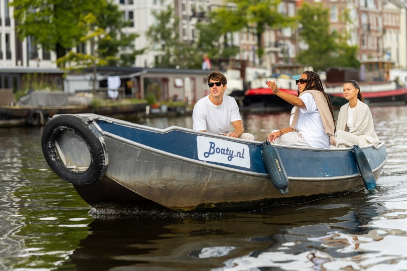 Drei Freunde gleiten in einem kleinen Mietboot durch einen Amsterdamer Kanal und genießen den Blick auf die Stadt.