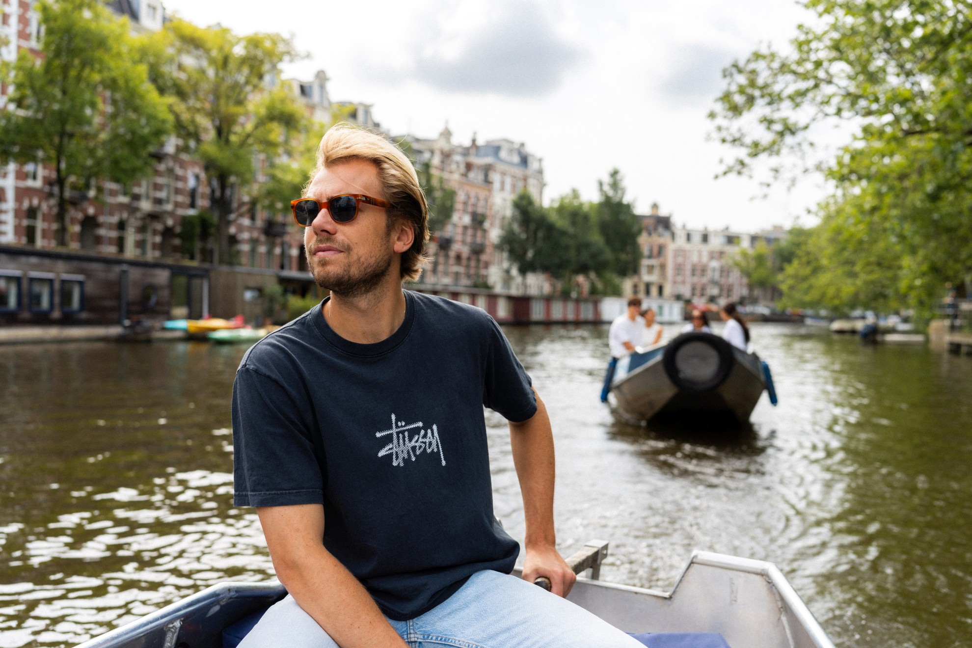 Ein Mann steuert ein Boot auf den Amsterdamer Grachten, und ein weiteres kleines Boot folgt ihm auf dem Wasser.